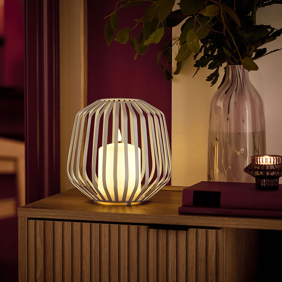 Uma vela LED num suporte de metal branco sobre uma cómoda de madeira.