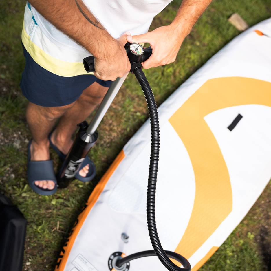 Homem a encher uma prancha de paddleboard insuflável com uma bomba manual.