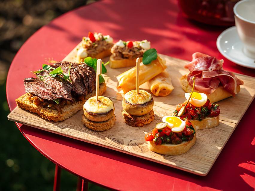 Variedade de tapas e canapés, incluindo bife, cogumelos, rolinhos primavera e bruschetta.
