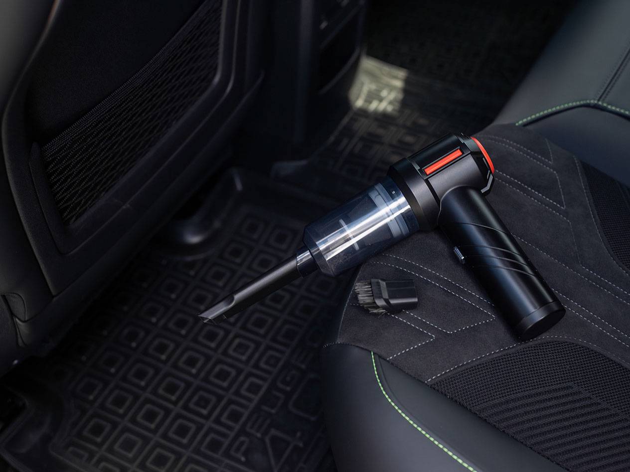 Aspirador de mão compacto com acessórios num banco de carro.