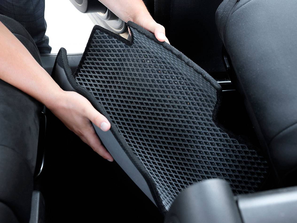 Pessoa a colocar um tapete de carro de borracha preta com padrão de diamante no interior de um veículo.
