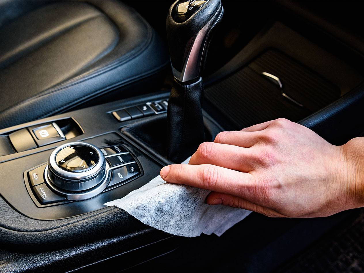 Mão a limpar o interior de um carro com um toalhete húmido.