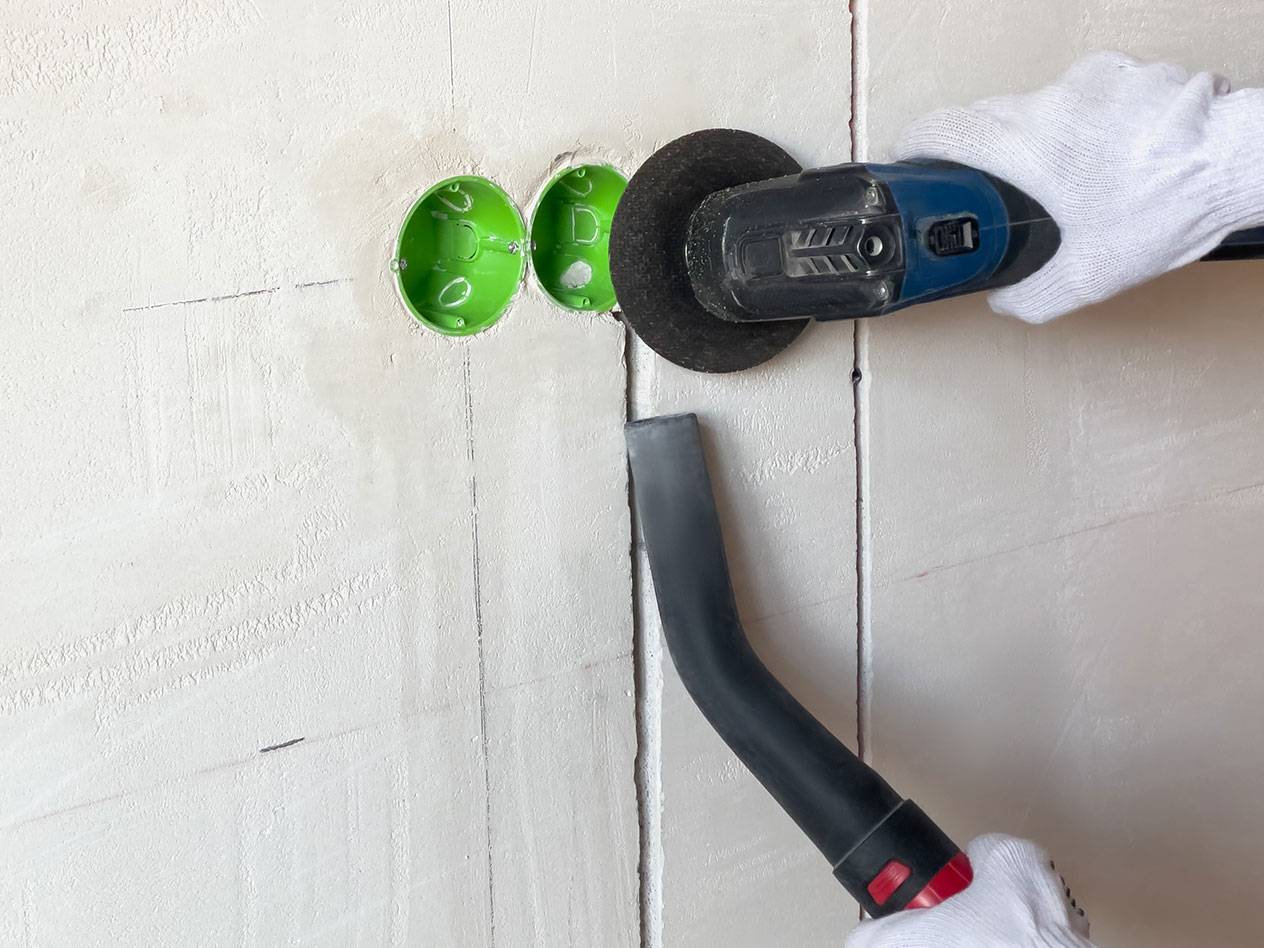 Ferramenta elétrica cortando ranhuras numa parede com um aspirador de pó.