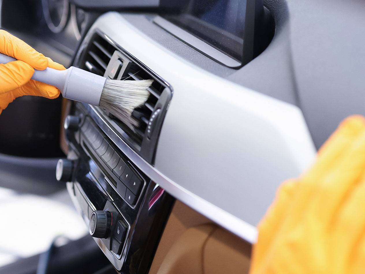 Limpeza do interior de um carro com uma escova de detalhe e luvas de borracha.