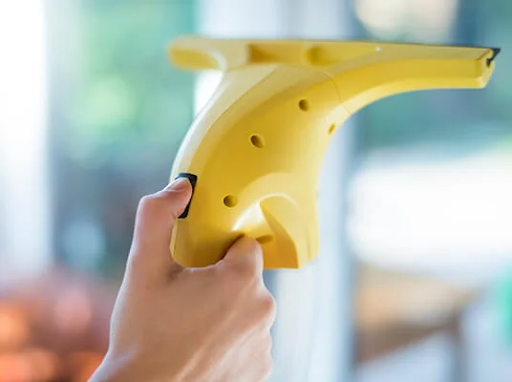 Mão segurando um limpa-vidros elétrico amarelo, limpando uma janela.