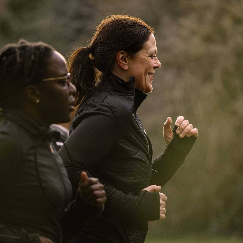 Duas mulheres em roupa desportiva a correr ao ar livre, uma a sorrir.