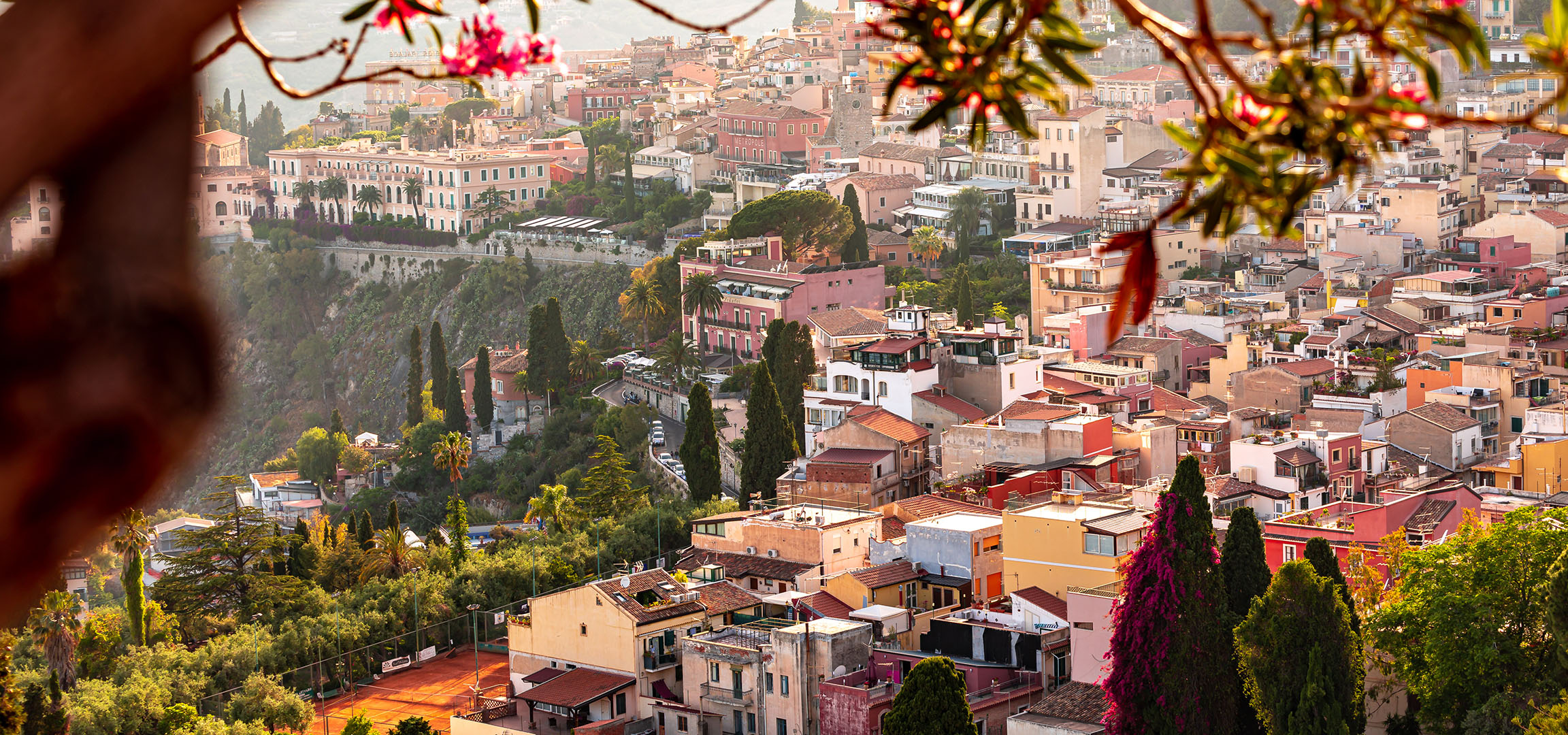 Vista panorâmica de uma cidade mediterrânica com edifícios coloridos e vegetação.