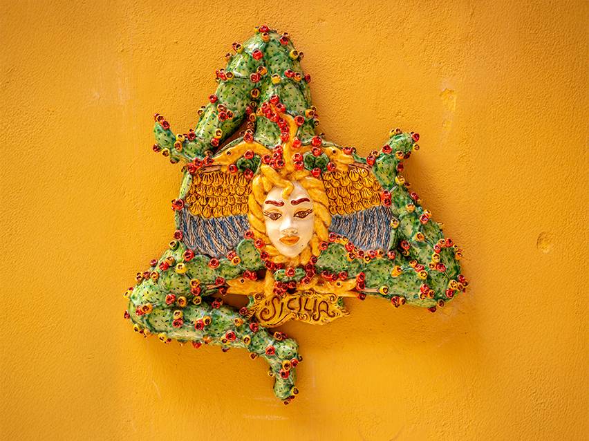 Decoração de parede siciliana em cerâmica com a Trinacria num muro amarelo.