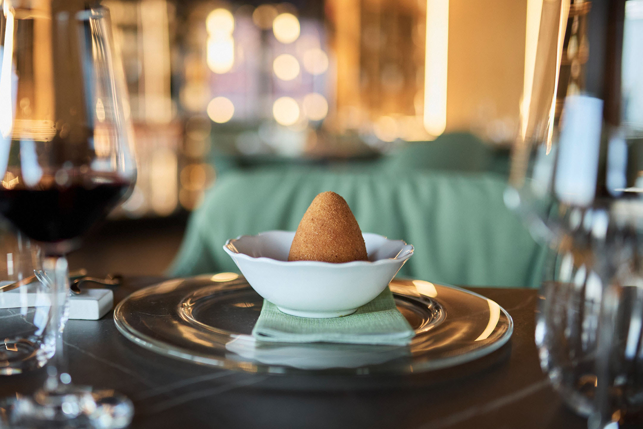 Arancini dourado numa tigela branca numa mesa de restaurante elegante.