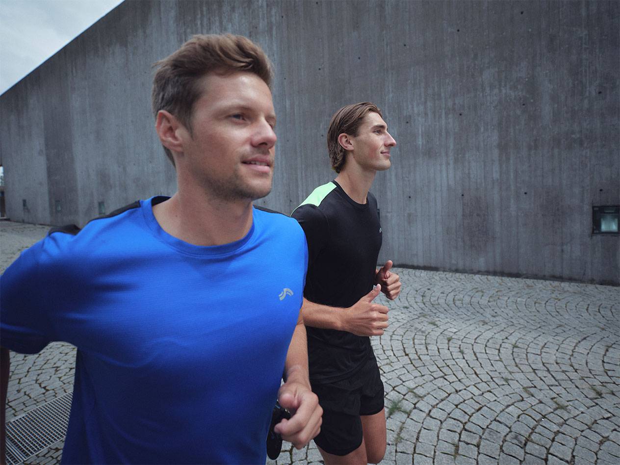 Dois homens a correr com t-shirts e calções desportivos, um azul e um preto.
