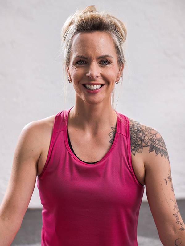 Uma mulher sorridente com um top esportivo rosa e tatuagens no ombro.