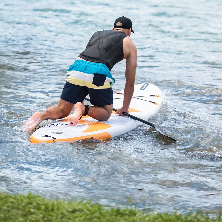 Homem de joelhos numa prancha de paddleboard com remo na água.
