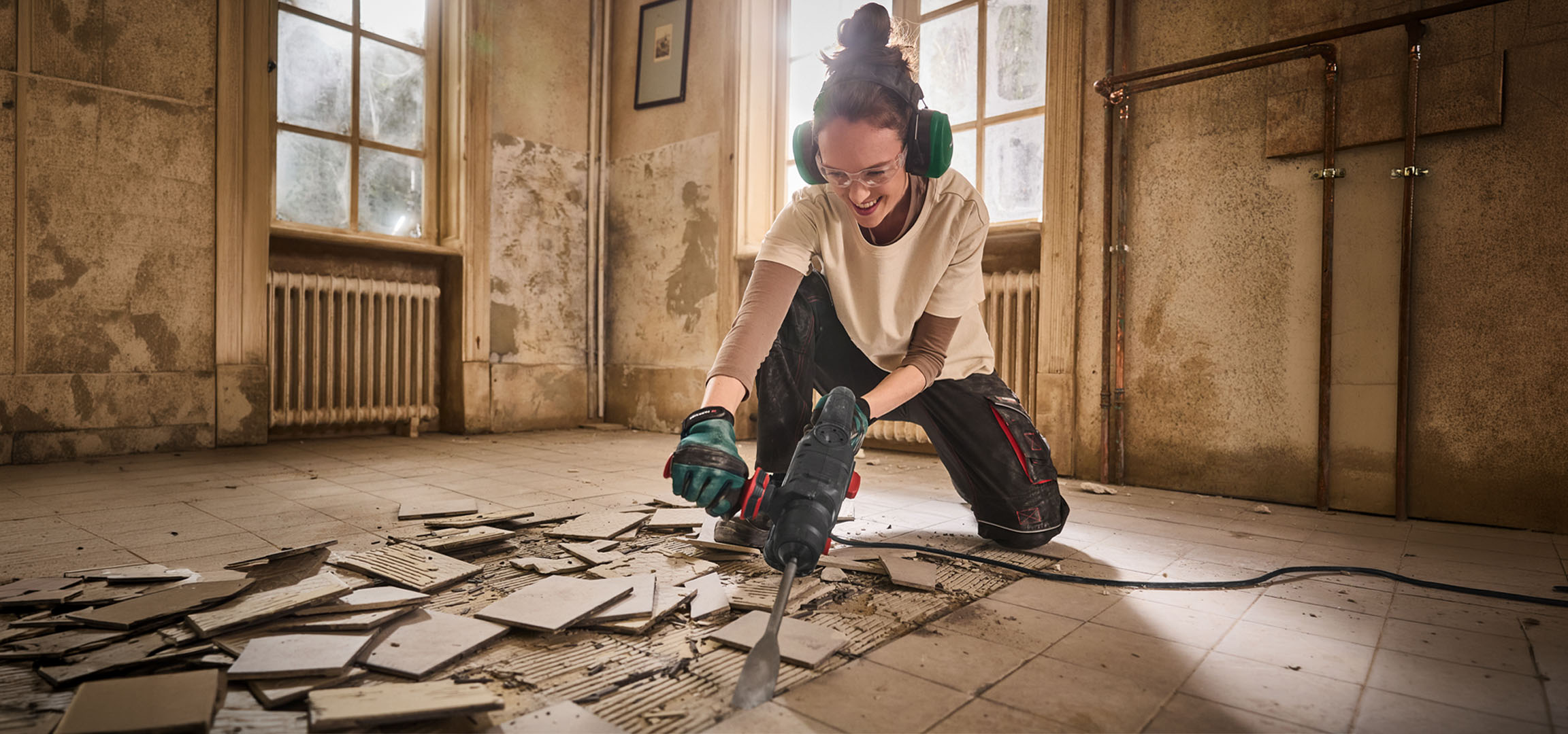 Mulher a usar um martelo demolitor para remover azulejos do chão numa sala antiga