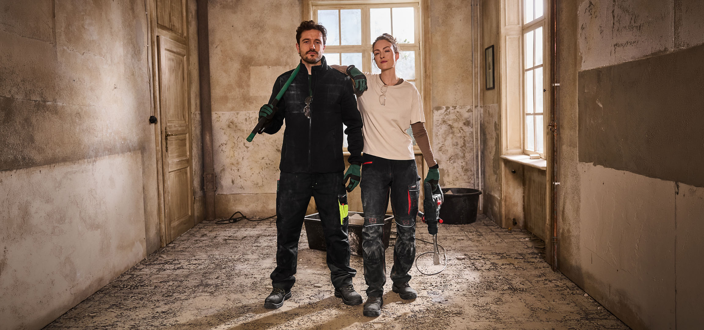 Dois trabalhadores da construção civil com roupa de trabalho e ferramentas num estaleiro.