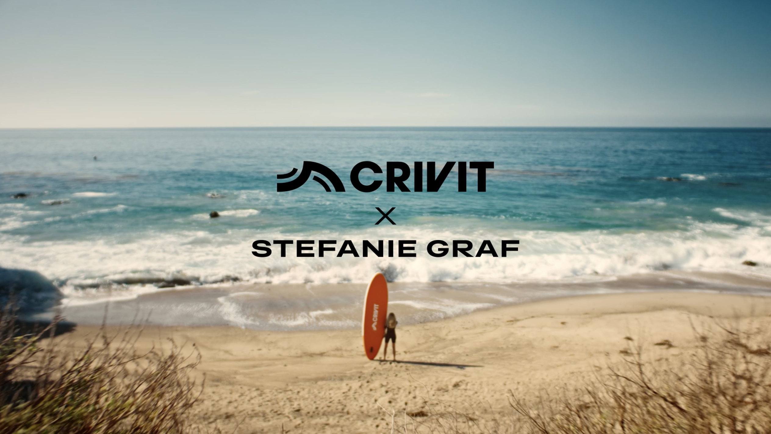 Mulher com prancha de SUP laranja numa praia de areia, com o mar ao fundo.