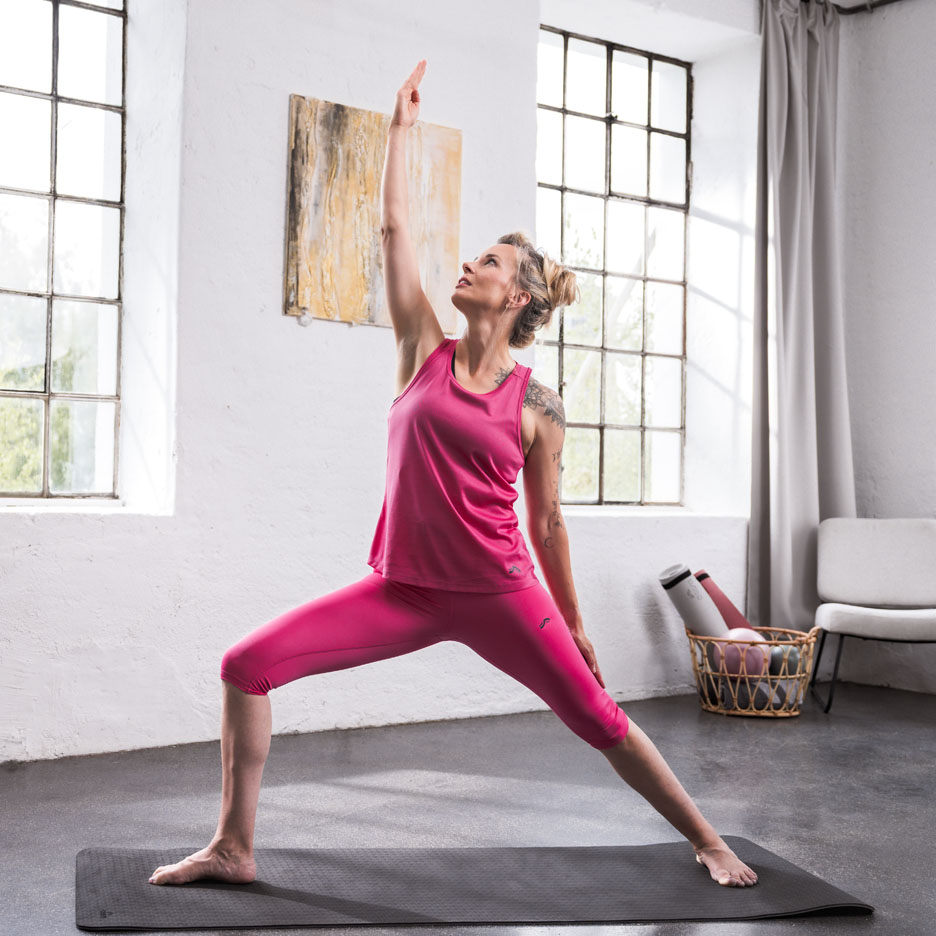 Mulher praticando yoga vestindo roupa esportiva rosa em um quarto claro.