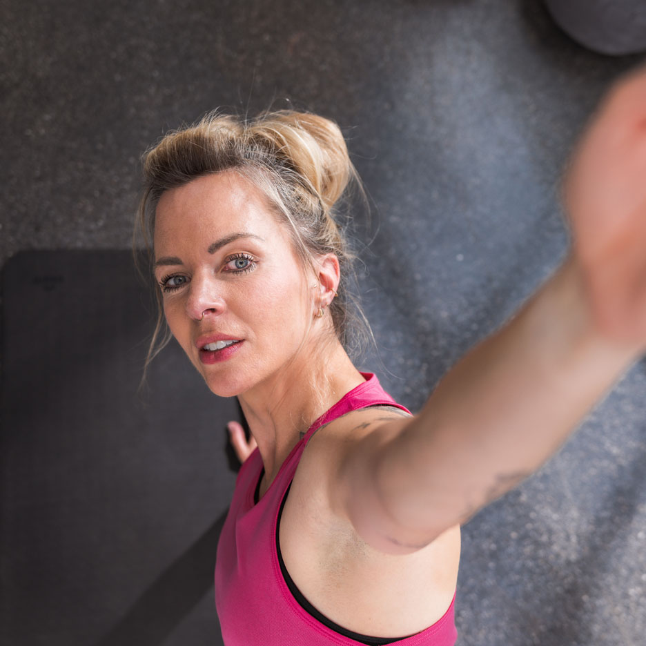 Uma mulher de top esportivo rosa tira uma selfie na academia.