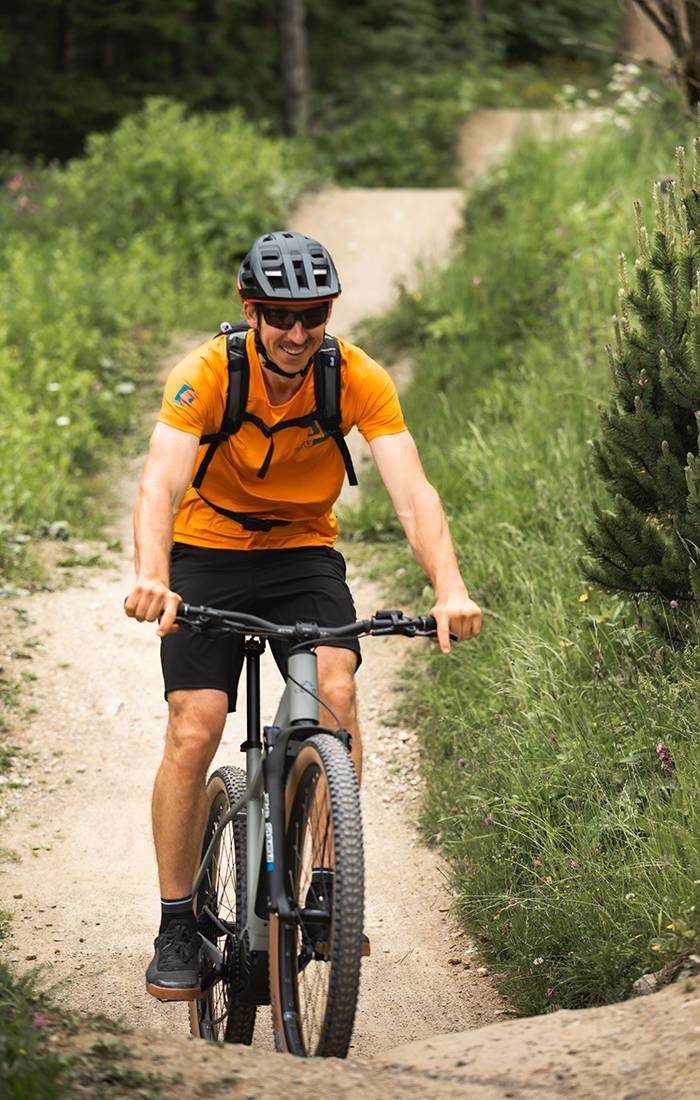Um homem sorri enquanto anda de bicicleta de montanha numa trilha.
