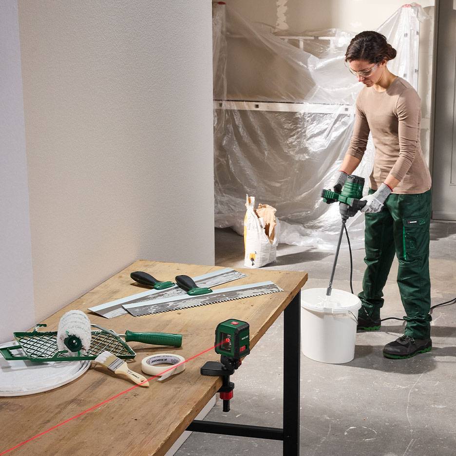 Mulher a misturar material de construção com ferramentas de pintura e nivelamento numa mesa.