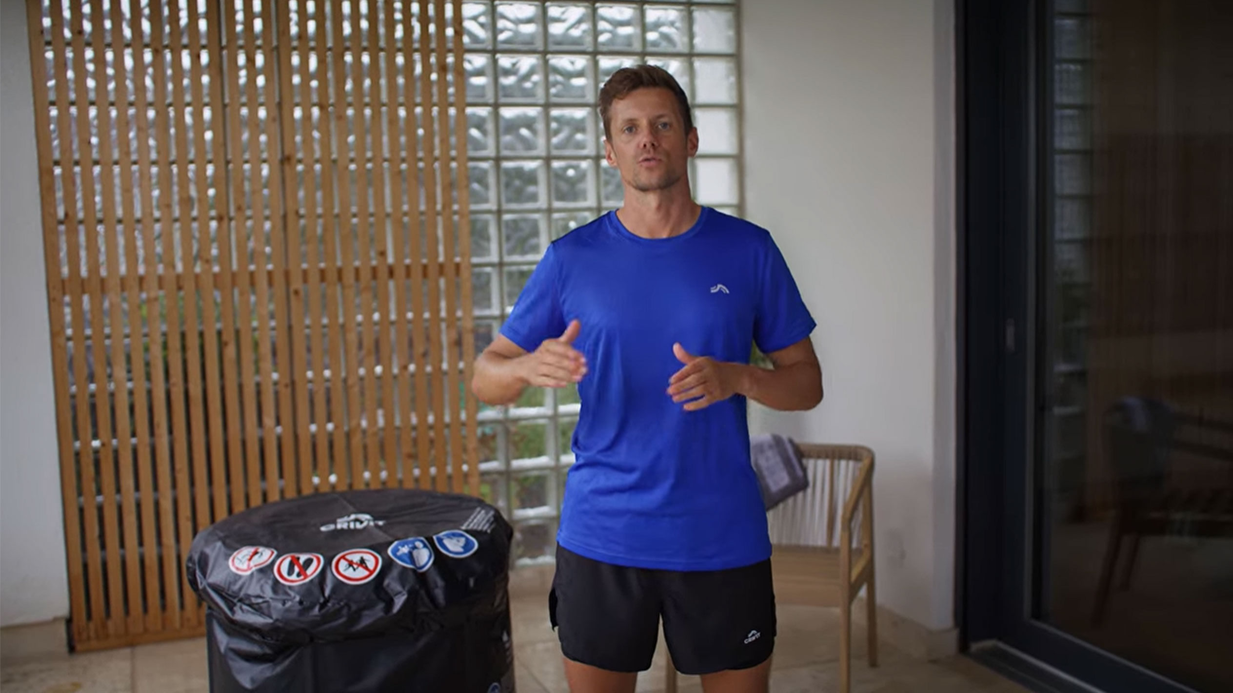 Homem de t-shirt azul e calções pretos, ao lado de uma capa preta de jacuzzi.