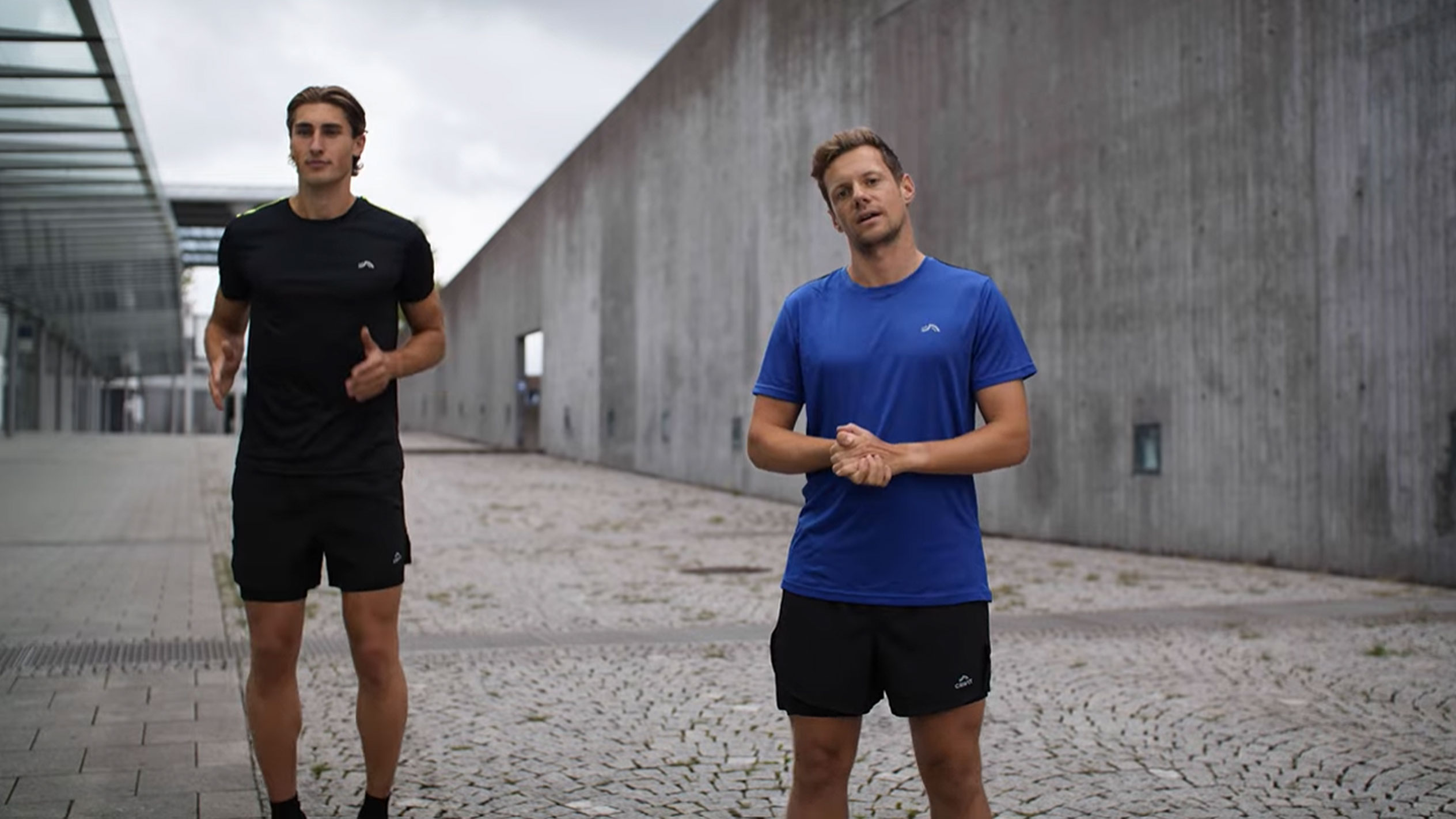 Dois homens em roupa desportiva preta e azul ao ar livre.