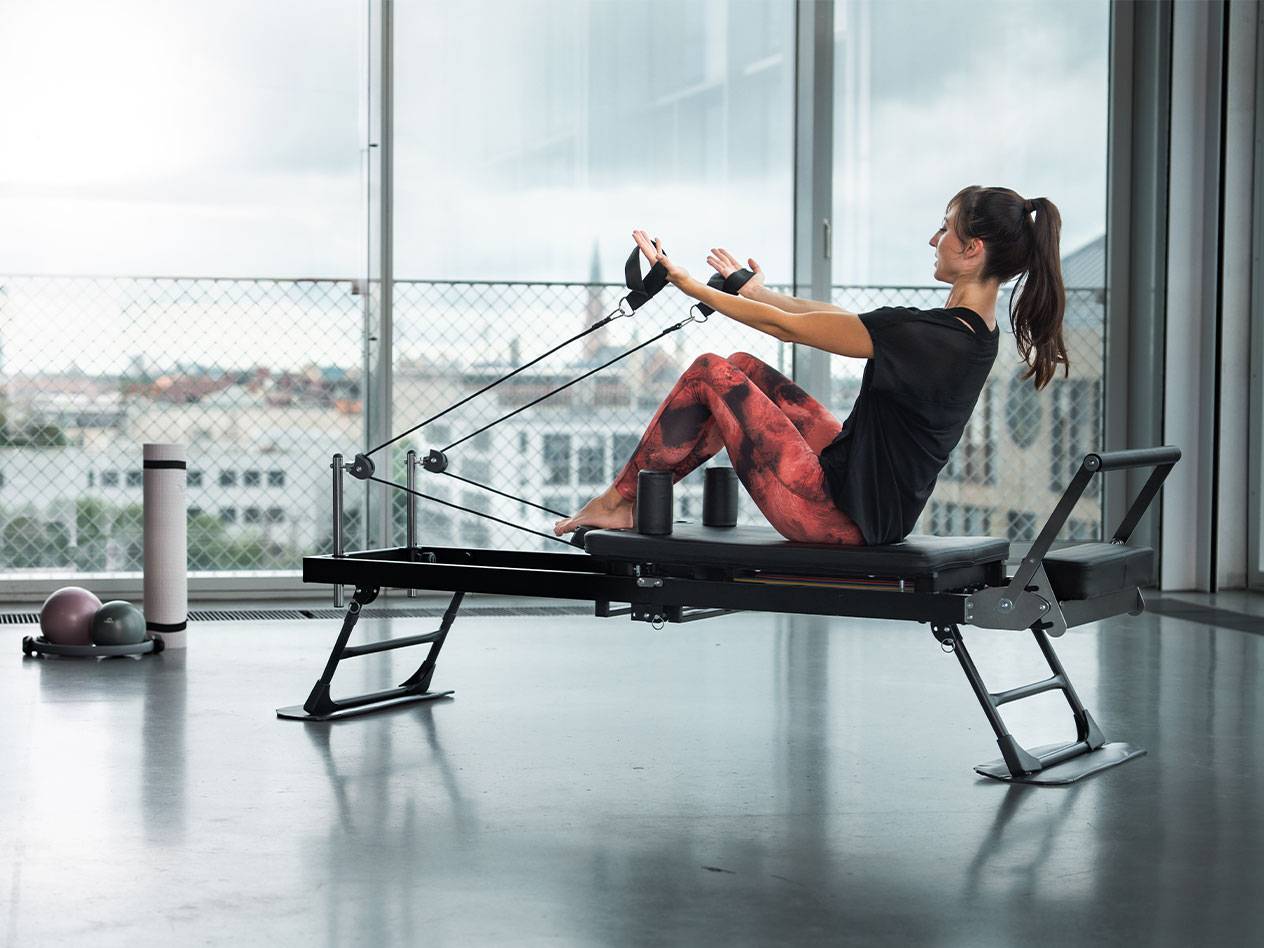 Mulher a fazer Pilates num reformer com vista para a cidade.