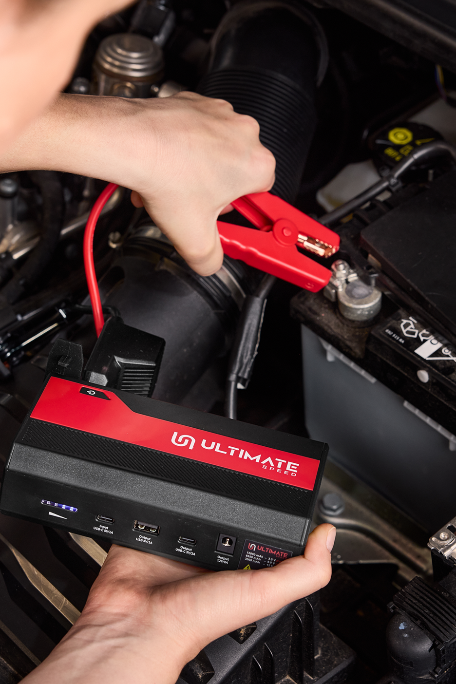 Pessoa a usar um arrancador de bateria portátil Ultimate Speed para ligar um carro.