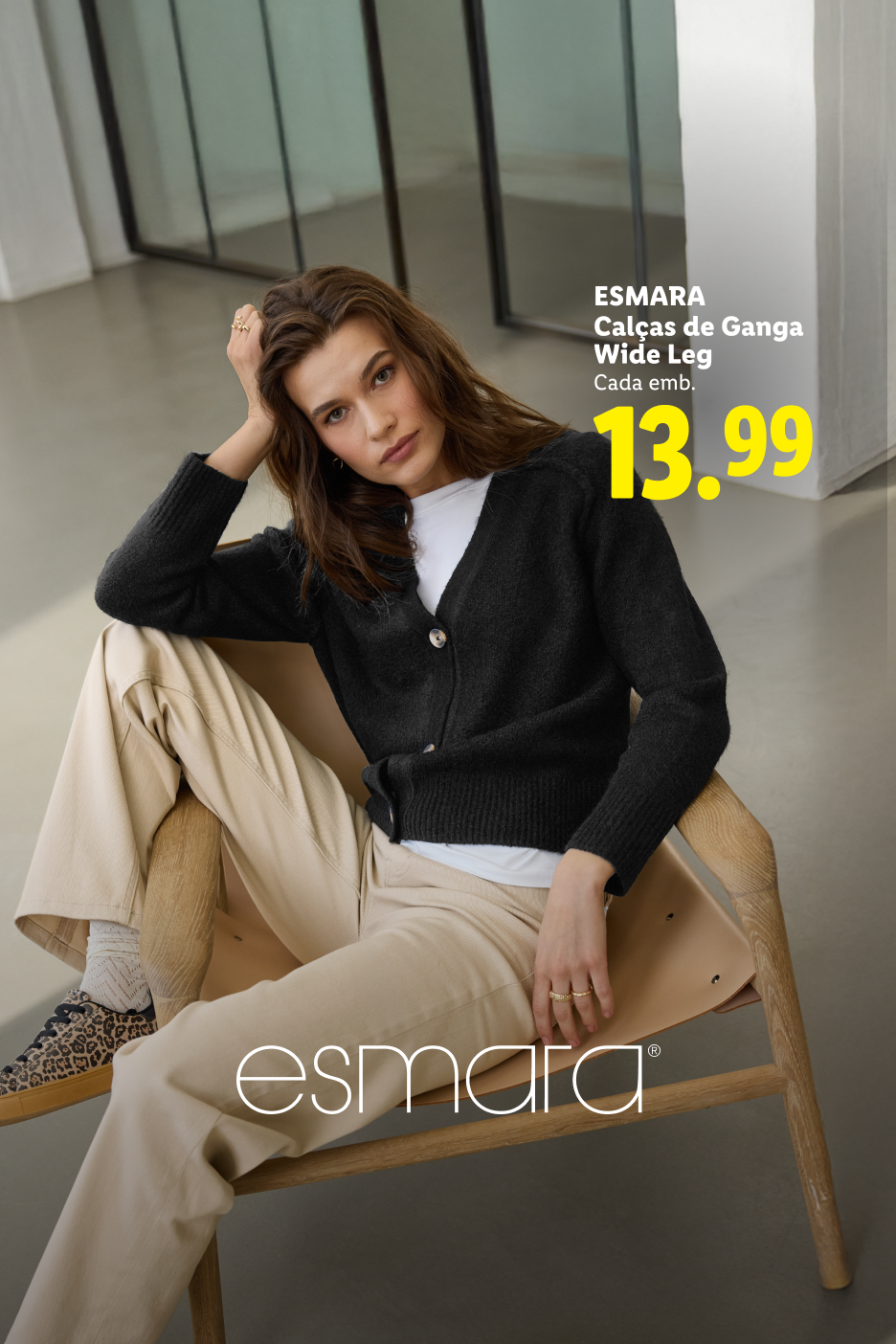 Mulher sentada a usar um casaco de malha preto e calças largas bege, com preço de 13,99.