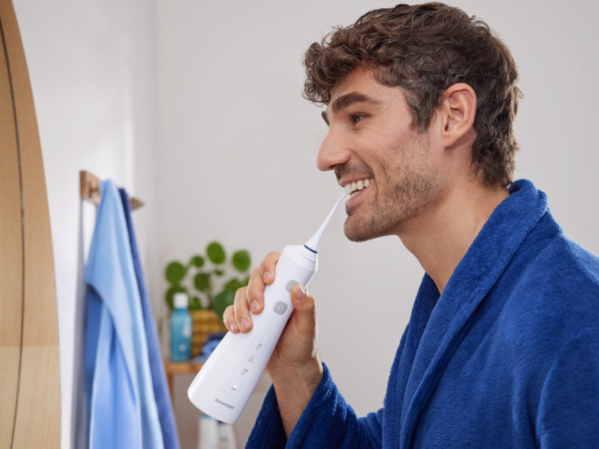 Um homem usa um irrigador bucal Braun Oral-B para limpar os dentes.