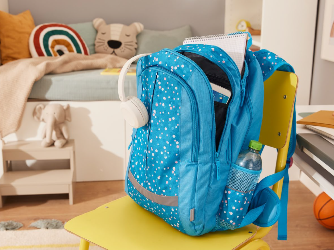 Mochila azul com bolinhas brancas e rosa, fones de ouvido brancos e garrafa de água em um quarto infantil.