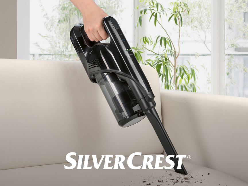 Aspirador de mão SilverCrest sendo usado para limpar um sofá.