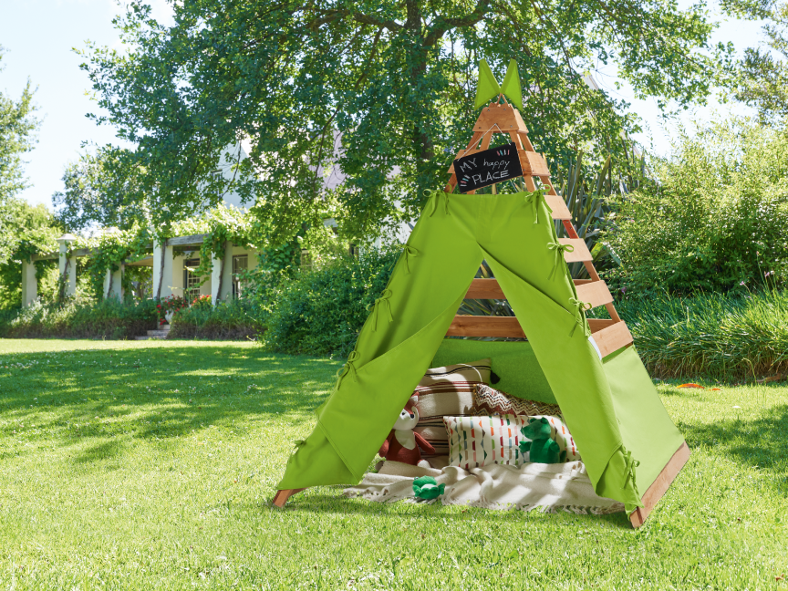 Uma tenda de brincar verde com almofadas e brinquedos em um gramado ensolarado.