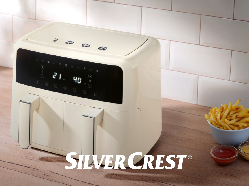 Fritadeira de ar creme SilverCrest com batatas fritas e molhos em uma bancada de madeira.