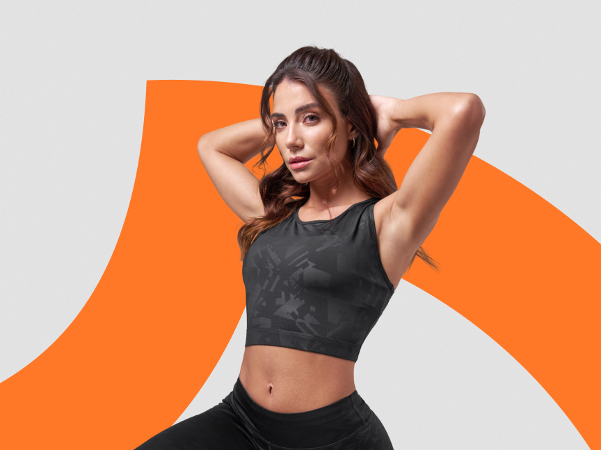 Mulher em top e calças de ginástica pretos, com fundo cinza e laranja.