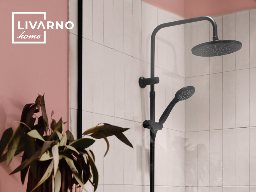 Chuveiro preto fosco com chuveirinho em um banheiro com azulejos brancos e parede rosa.