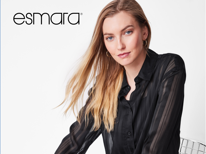 Uma mulher loira sorri, vestindo uma camisa preta transparente, com o logotipo da Esmarana parte superior esquerda.