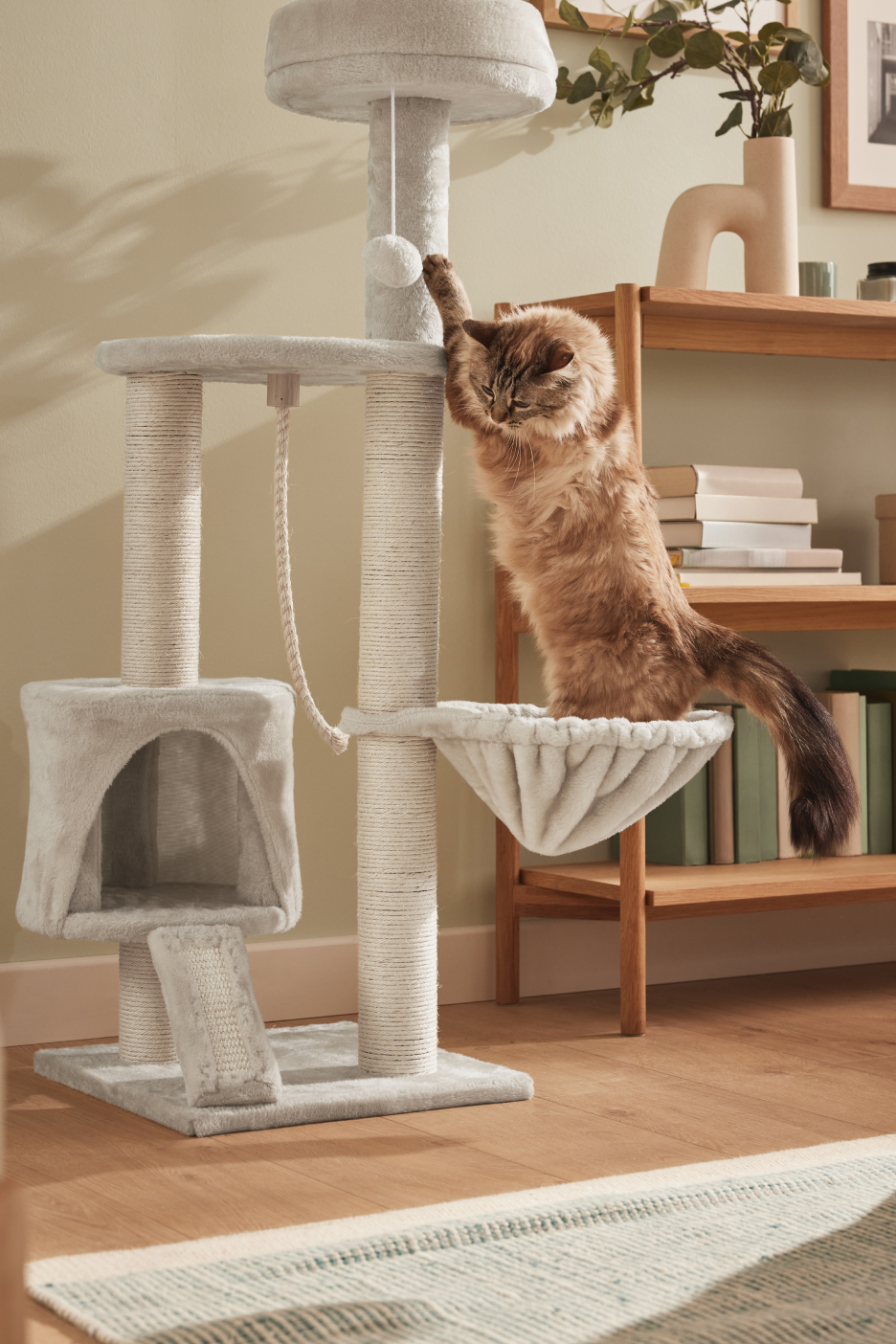Um gato marrom brincando em um arranhador cinza de vários níveis com uma cama e um brinquedo.
