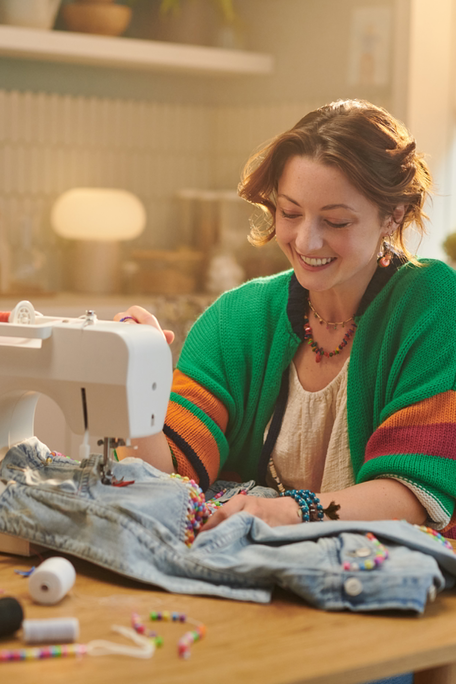 Mulher sorridente costurando jeans com miçangas coloridas em uma máquina de costura.