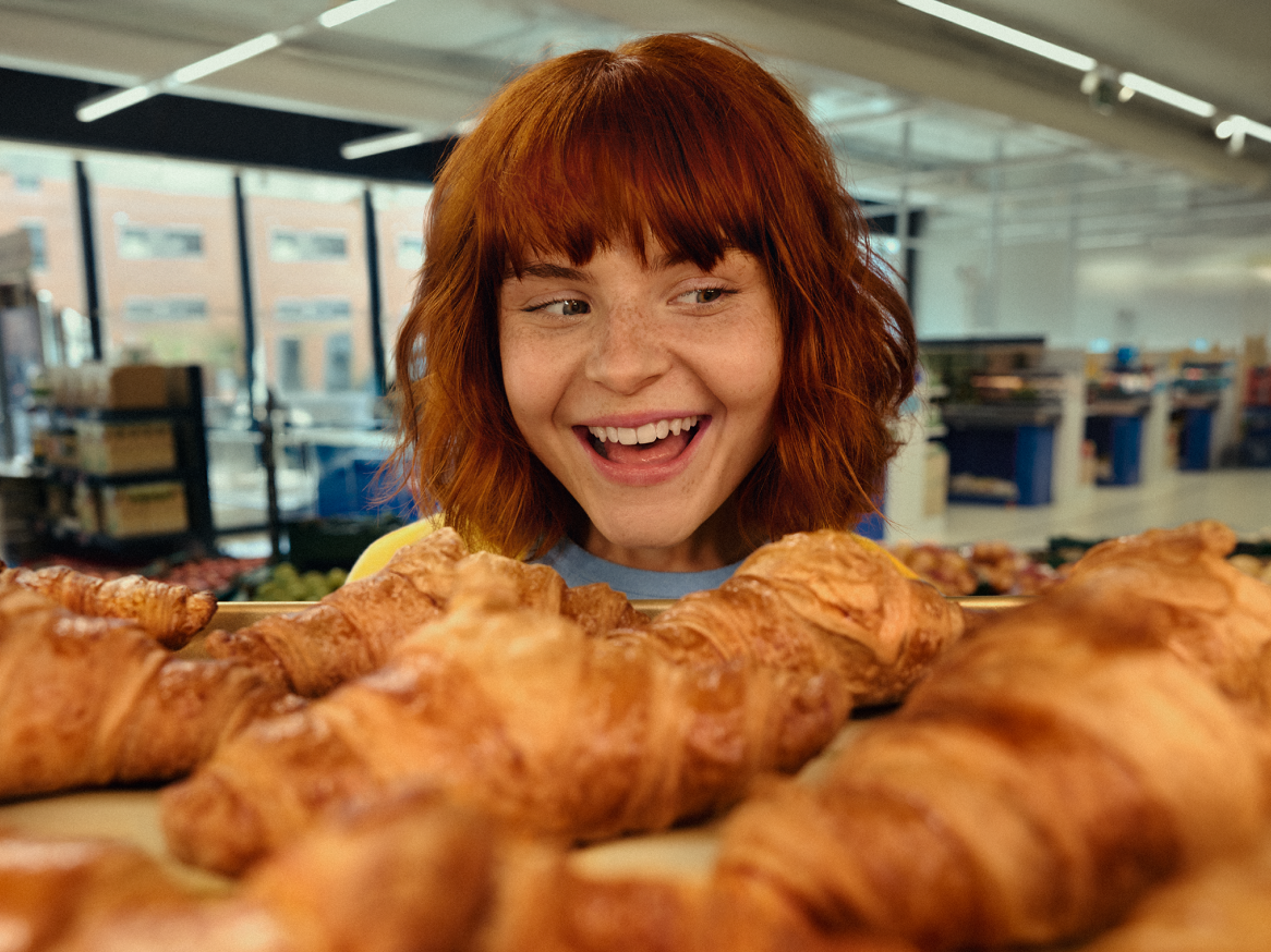 Mulher sorridente a olhar para croissants frescos numa padaria de supermercado.