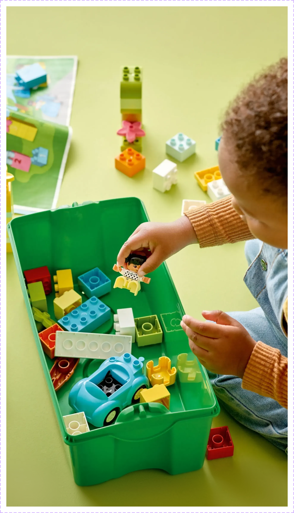Criança a brincar com peças de construção coloridas da caixa de blocos de construção LEGO Duplo.