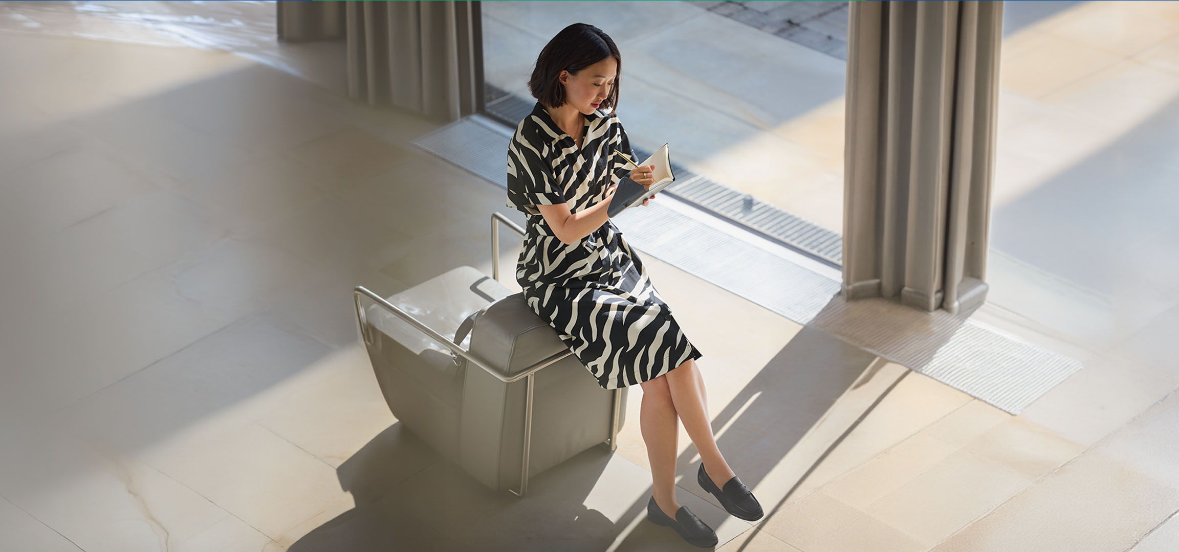 Mulher de vestido com estampa de zebra, sentada numa cadeira, a escrever num caderno.