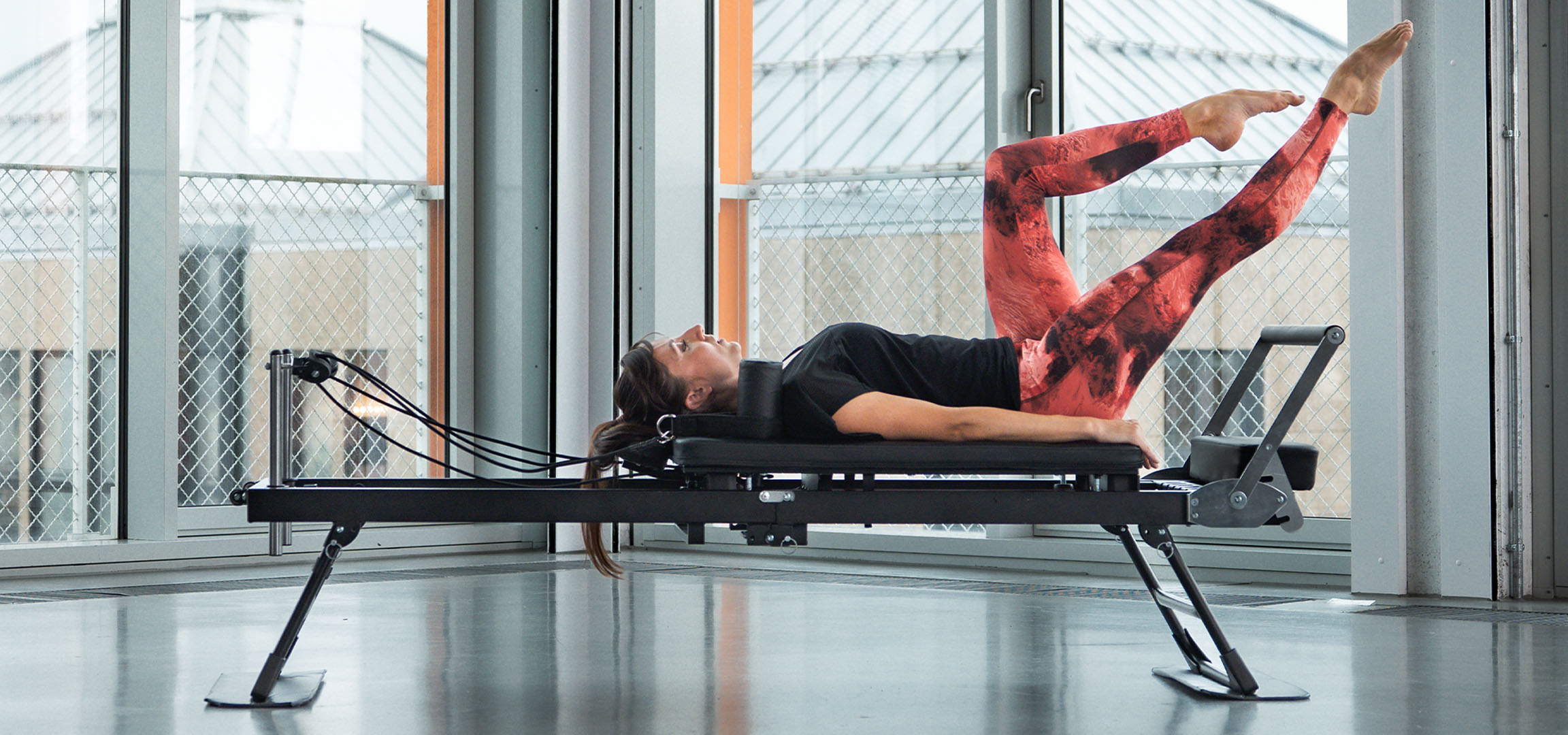 Mulher a fazer Pilates numa máquina reformer, com acessórios de fitness por perto.
