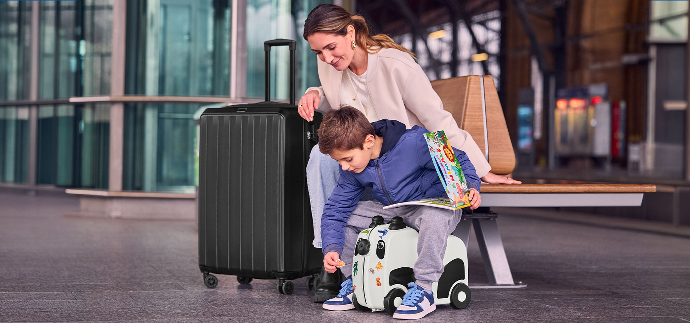 Mãe e filho com bagagem no aeroporto, criança a brincar com uma mala de viagem.