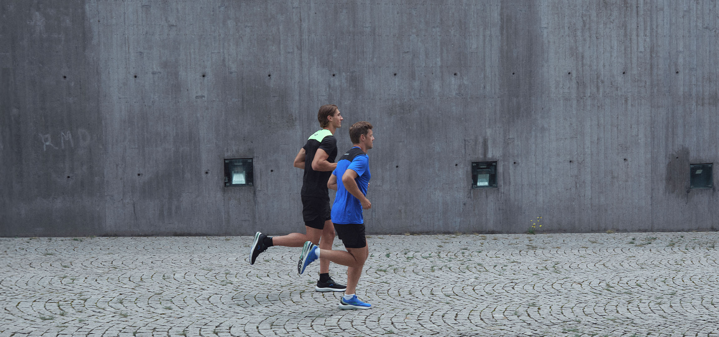 Dois homens em roupa desportiva a correr ao longo de uma parede.