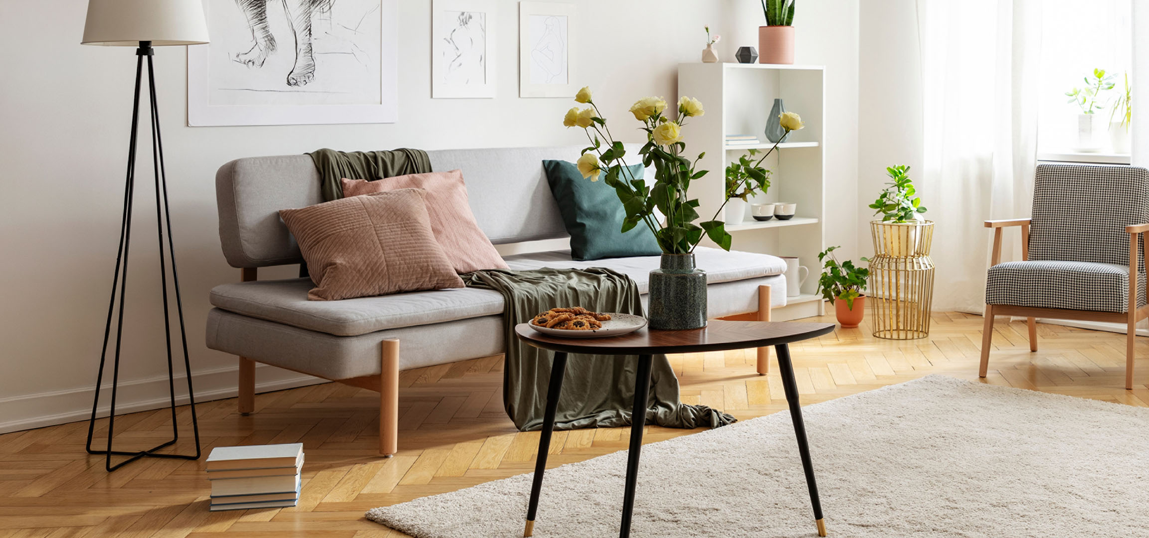 Sala de estar acolhedora com sofá cinzento, almofadas, mesa de centro com biscoitos e vaso de flores.