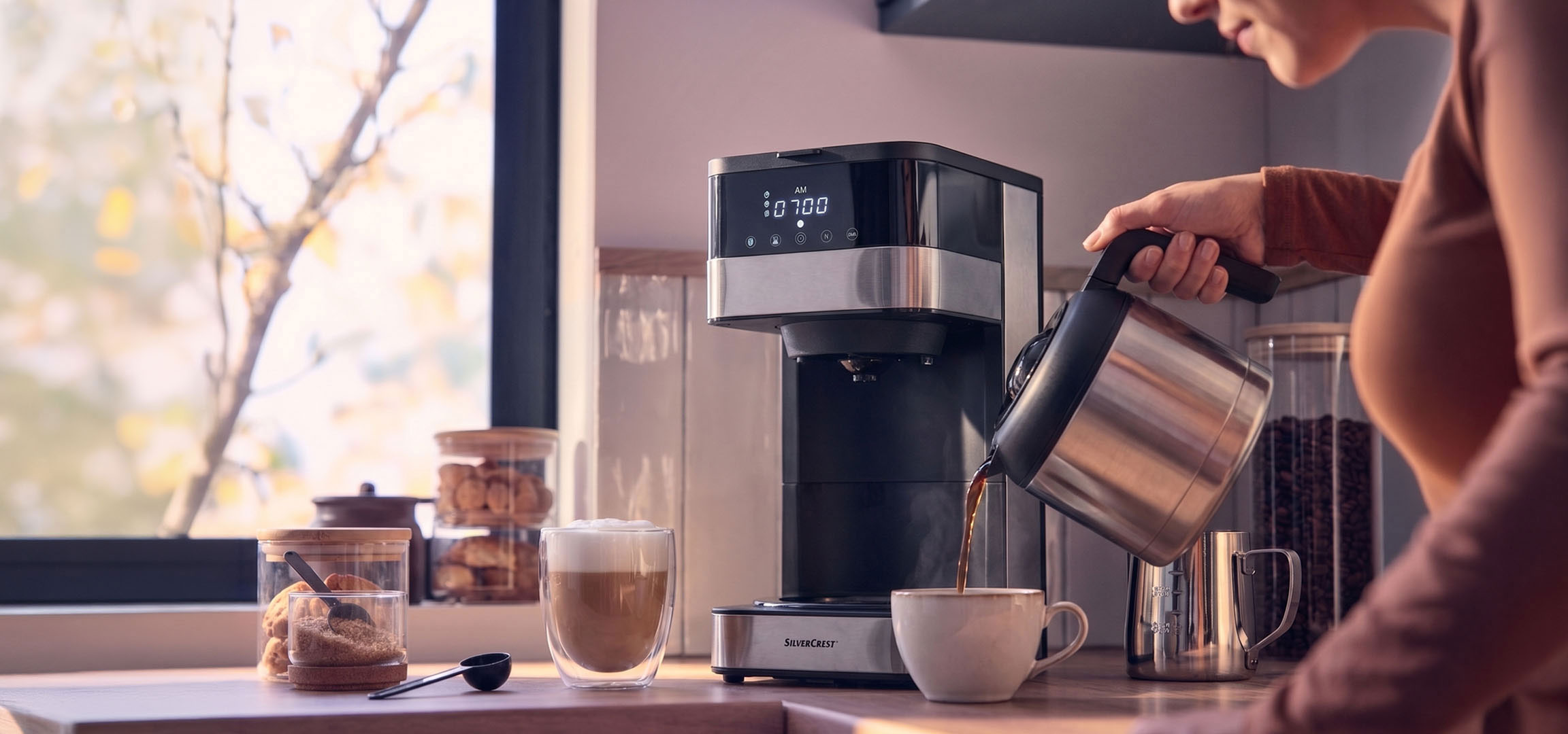 aiLabeling.aiLabelForImageAltText: Máquina de café a servir café numa chávena, com uma janela brilhante ao fundo.