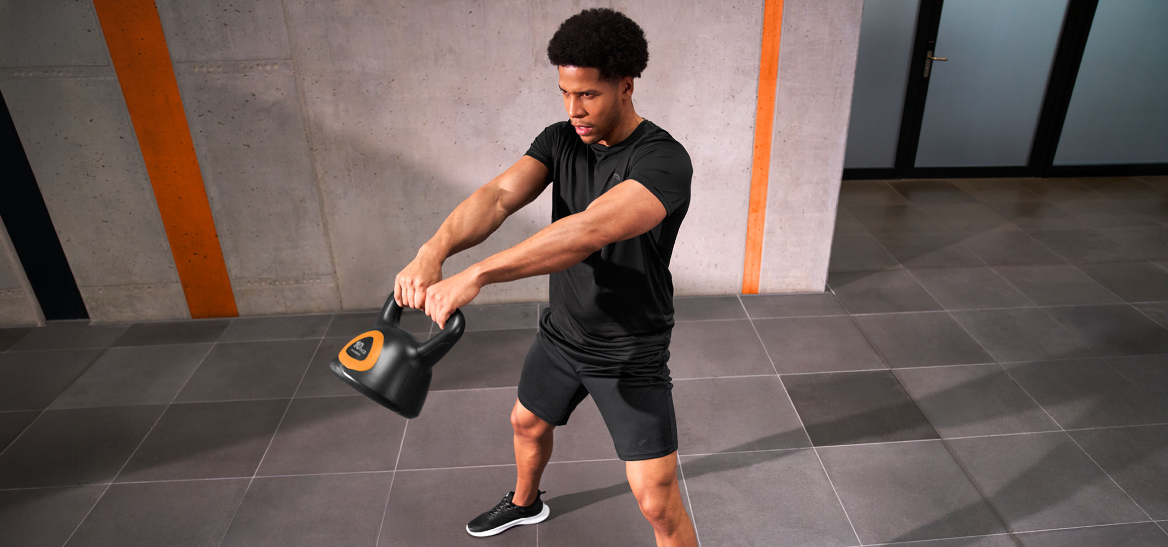 aiLabeling.aiLabelForImageAltText: Homem a treinar com um kettlebell preto e laranja.
