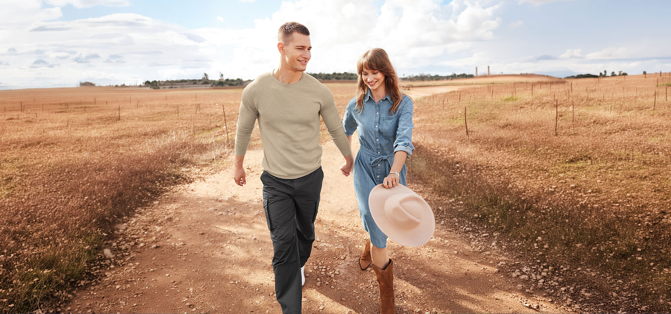 aiLabeling.aiLabelForImageAltText: Casal com roupa casual a caminhar por um caminho de terra num campo.