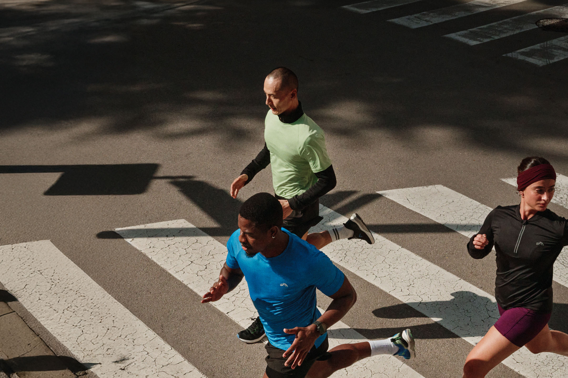 Três corredores em roupa desportiva a atravessar uma passadeira na cidade.