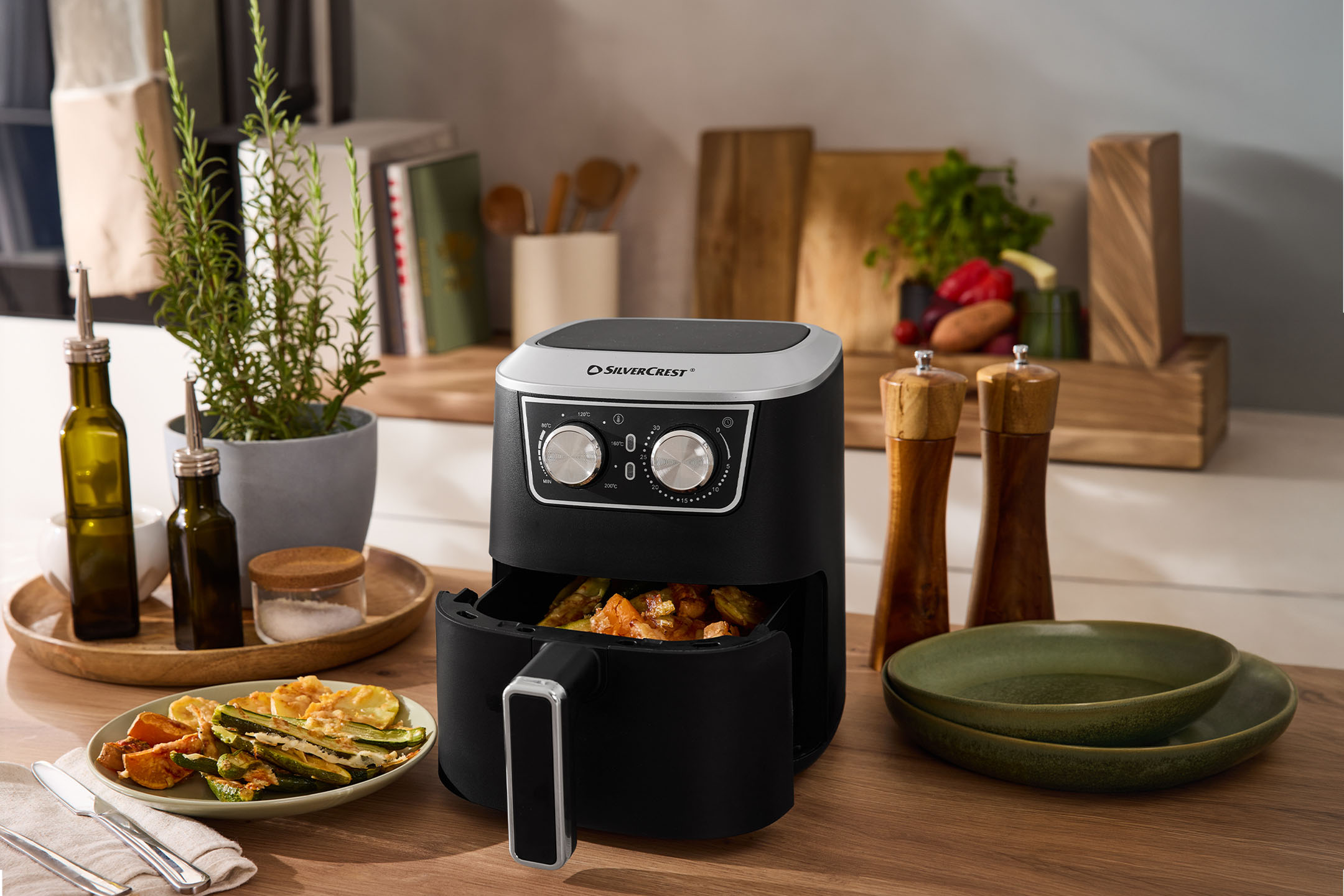 Fritadeira de ar com vegetais assados, azeite, sal e pimenta numa bancada de cozinha.